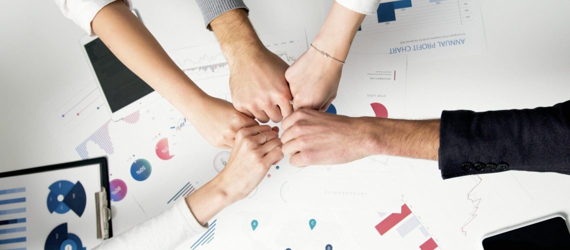 Free Colleagues celebrate success with a fist bump over financial charts depicting teamwork and unity. Stock Photo