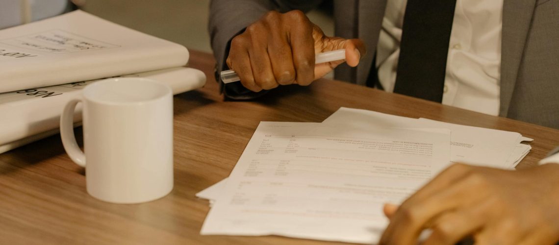 Free Close-up of a businessman holding and reviewing documents on a wooden desk. Stock Photo
