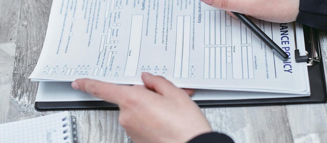 Free Close-up of hands analyzing insurance policy paperwork with pen on table. Stock Photo